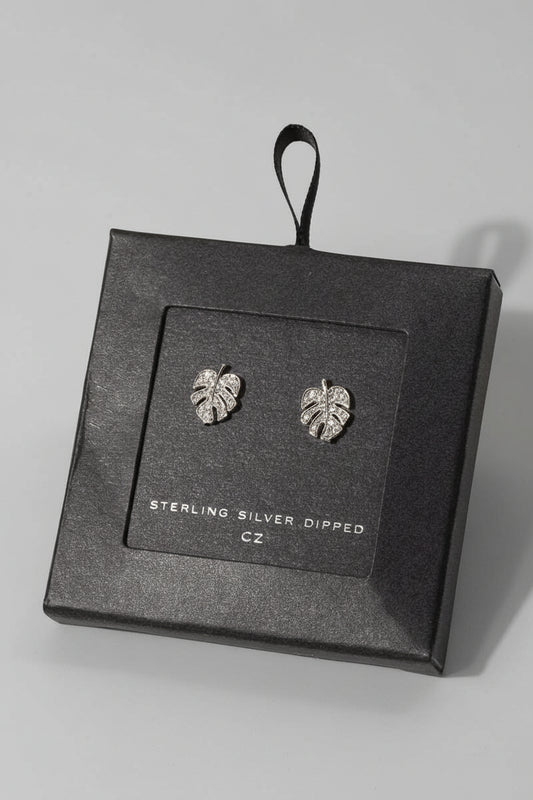 A pair of white gold dipped monstera leaf stud earrings presented in a black box with the brand name 'Secret Box' visible.