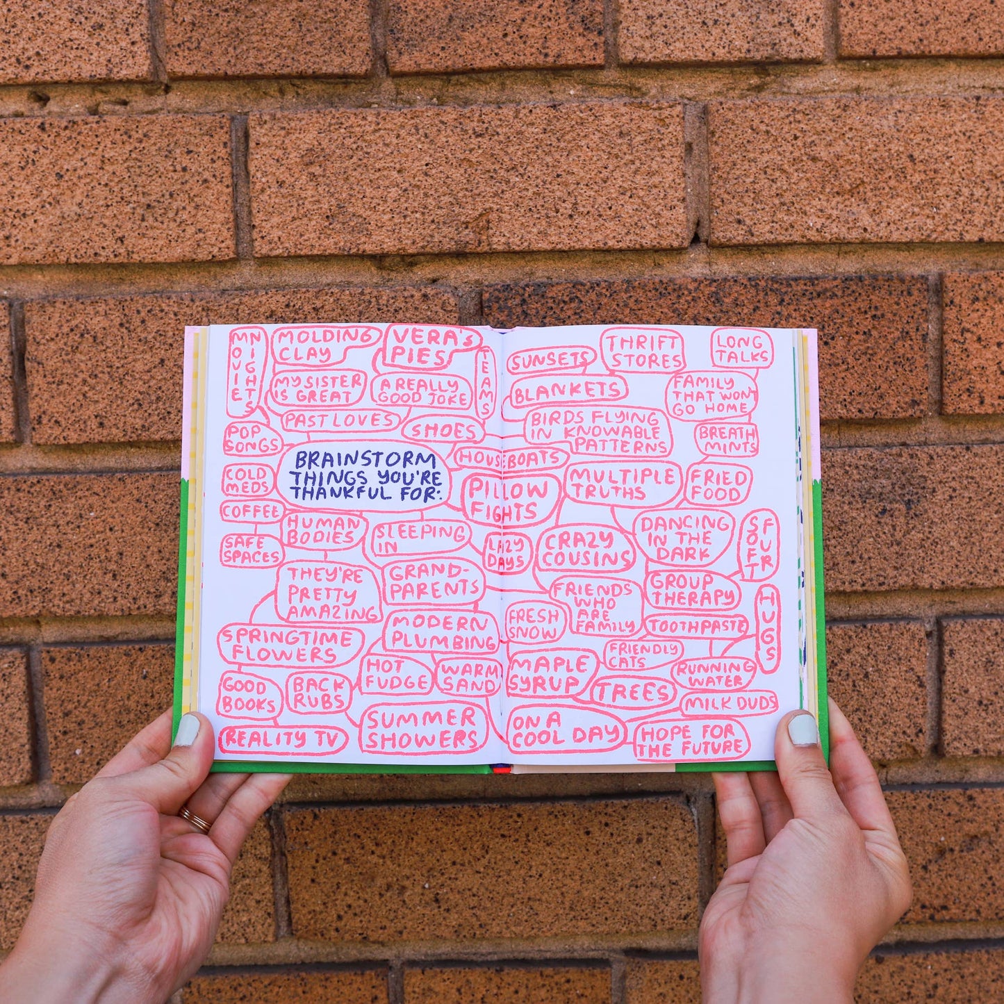 Hands holding a book open against a brick wall with text on the pages.