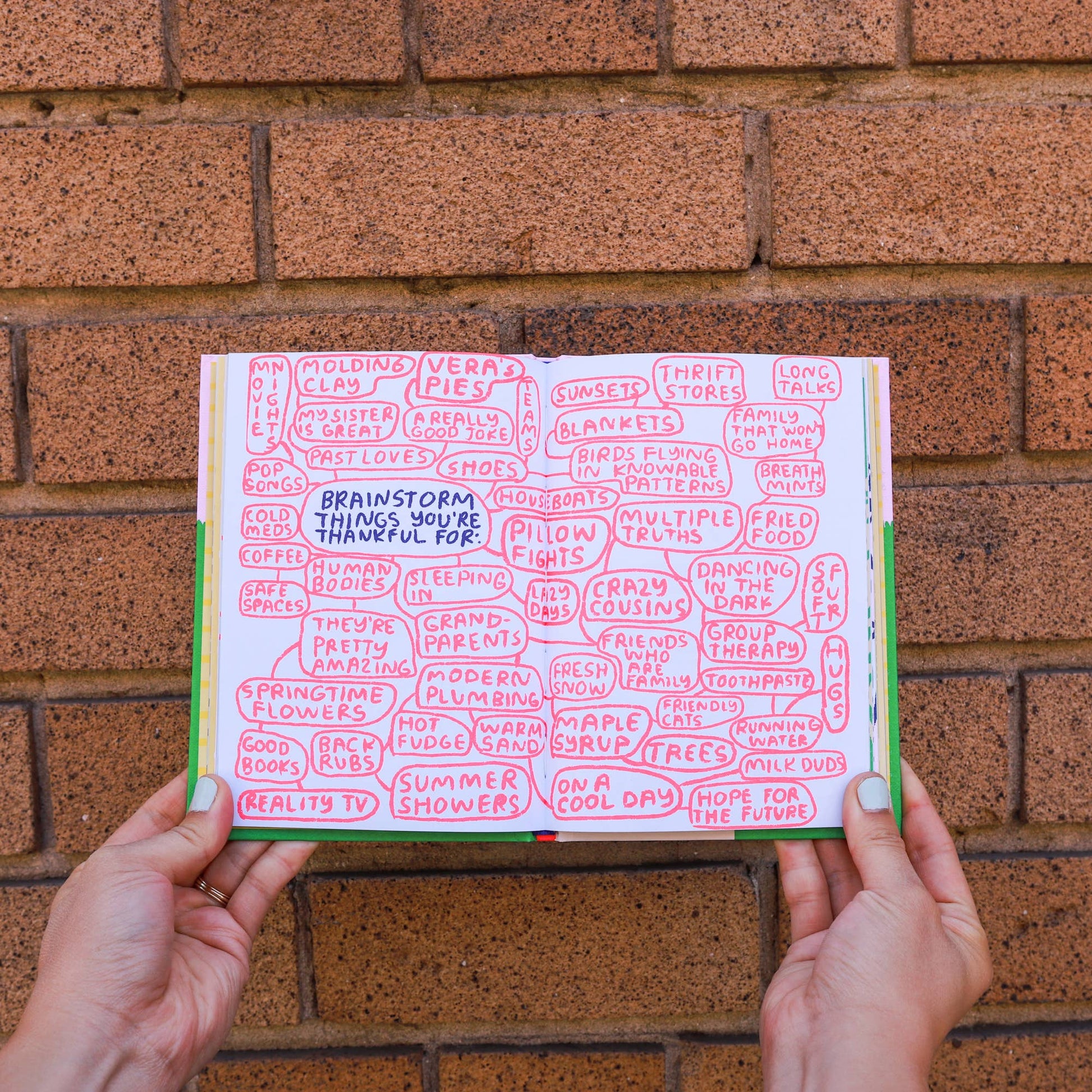 Hands holding a book open against a brick wall with text on the pages.