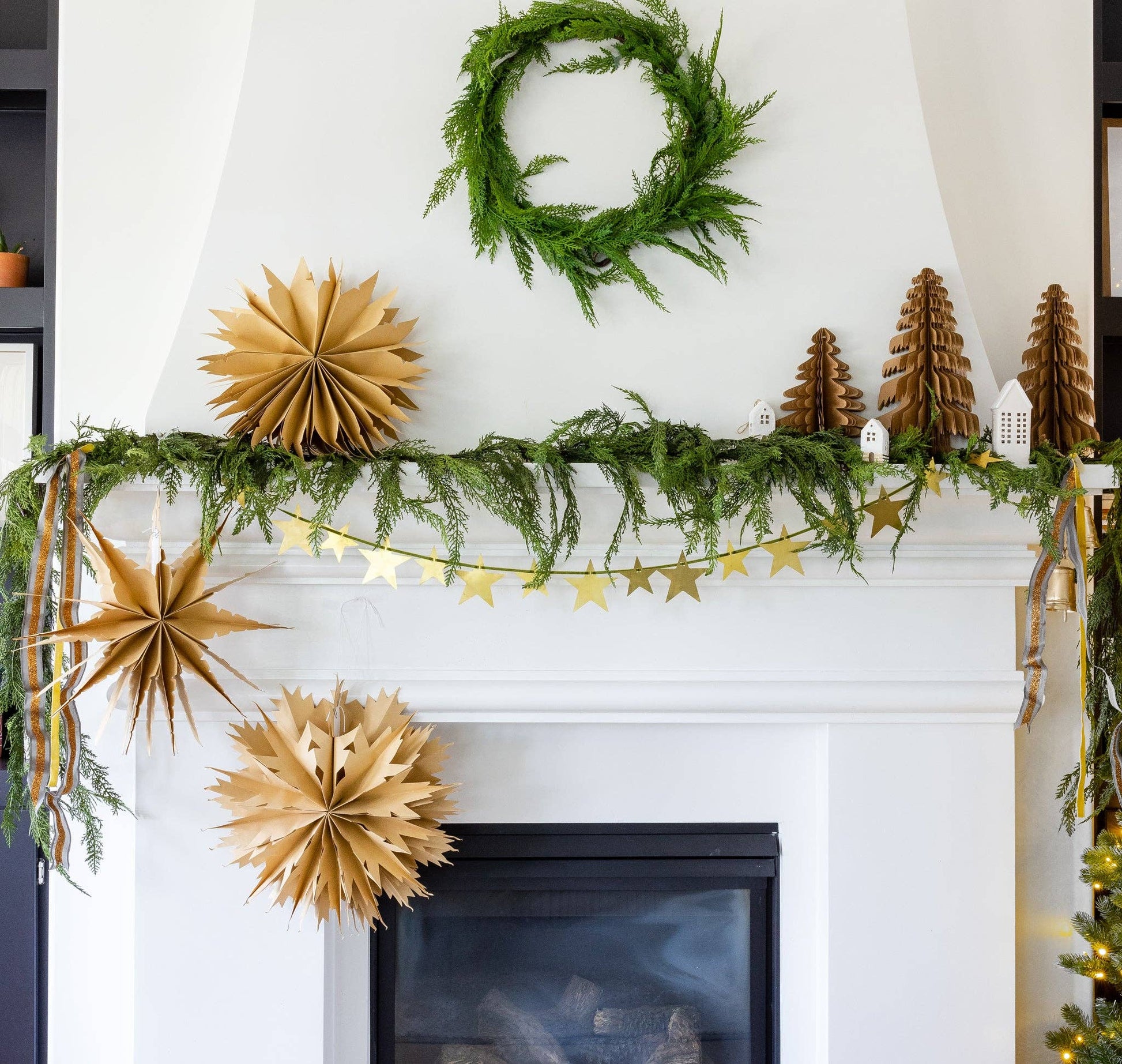 Decorative fireplace mantel with greenery, gold paper stars, and a wreath.