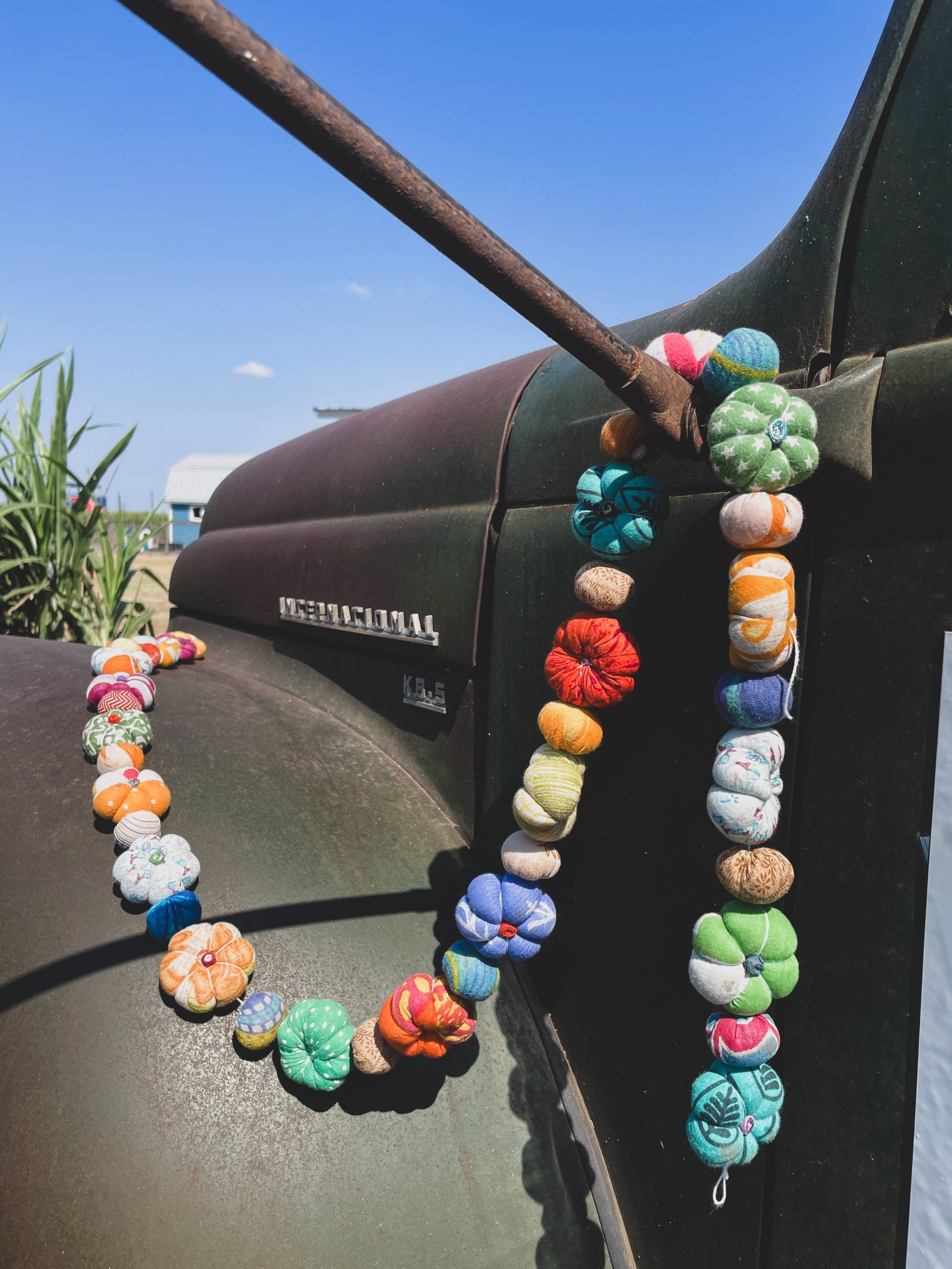 Colorful beaded necklace draped over a vehicle's rearview mirror with a clear blue sky in the background.