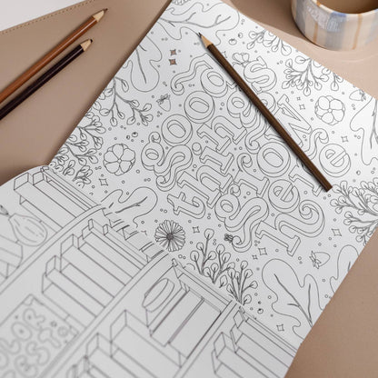 Coloring book with intricate patterns, a pencil, and a cup of coffee on a table.