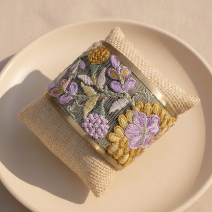 Floral embroidery cuff bracelet shown on a woven texture pillow on a neutral background