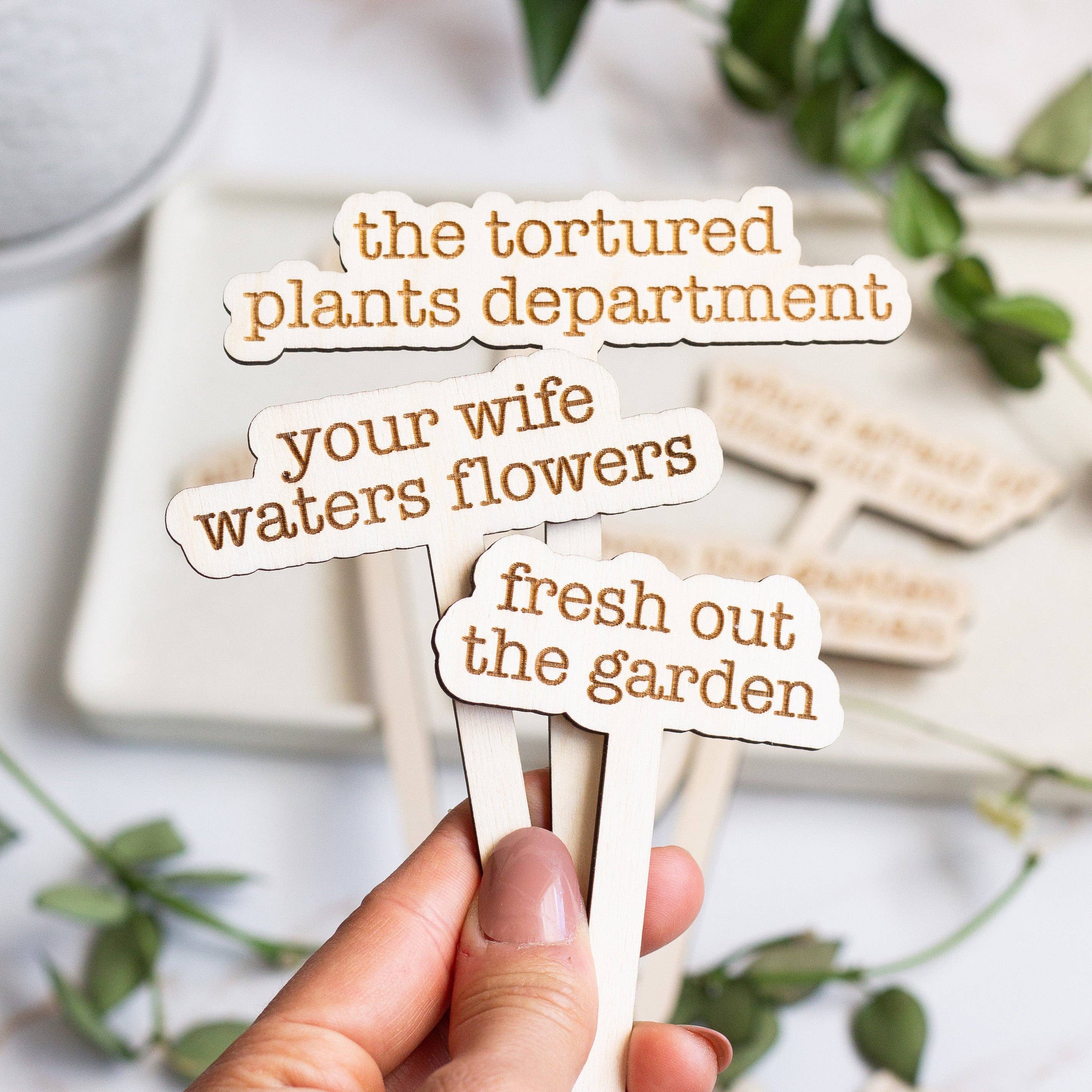 A wooden plant marker laser-engraved with 'The Tortured Plants Department,' crafted from unfinished Baltic Birch Plywood.