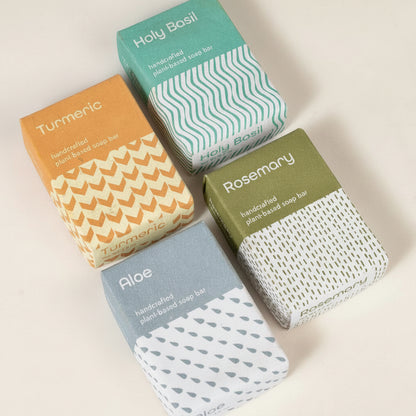 Four soap bars in different packaging with visible branding on a white background