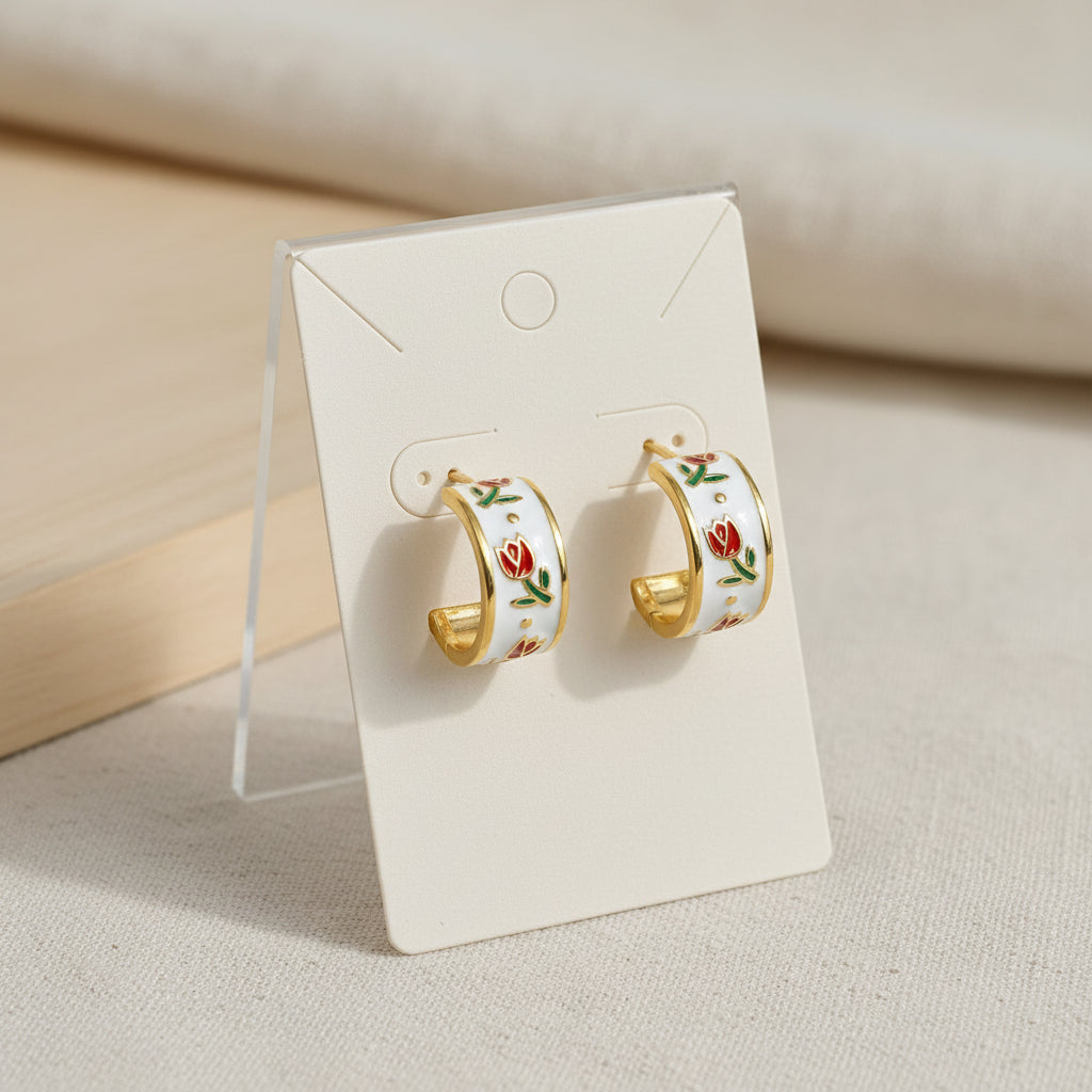 Gold hoop earrings with red rose designs on a white stand.