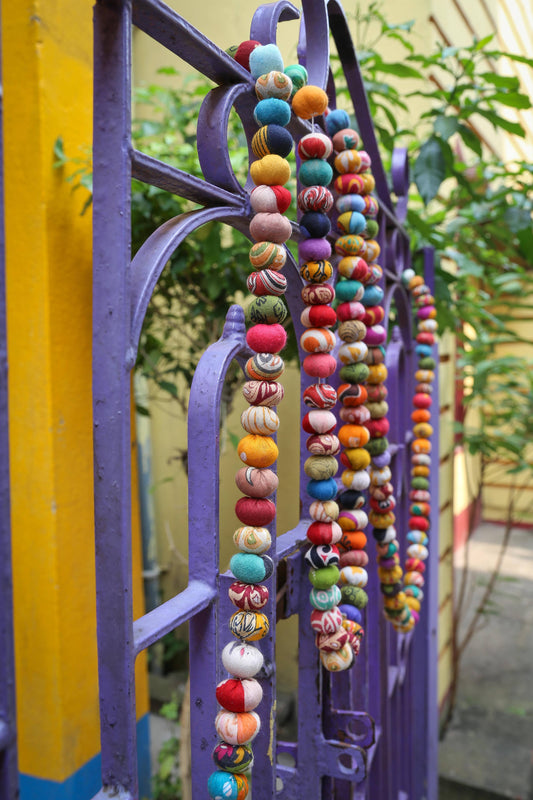 Colorful beaded necklace hanging on a purple metal gate with blurred greenery in the background