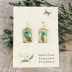 Rectangular resin earrings with turquoise dried flowers and gold trim on a display card
