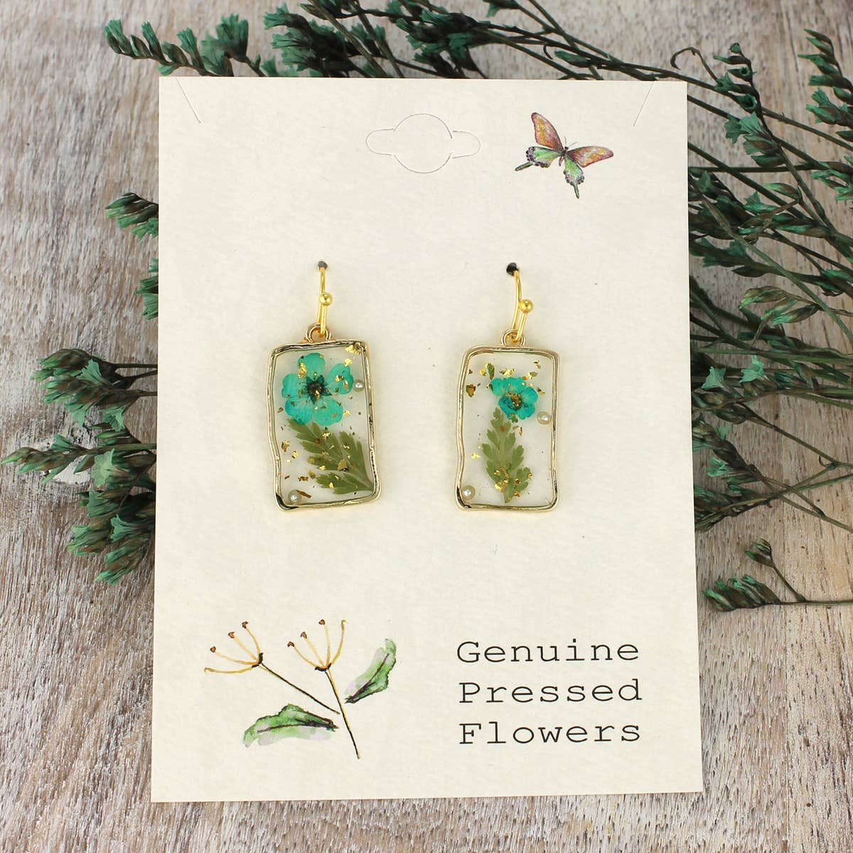Rectangular resin earrings with turquoise dried flowers and gold trim on a display card
