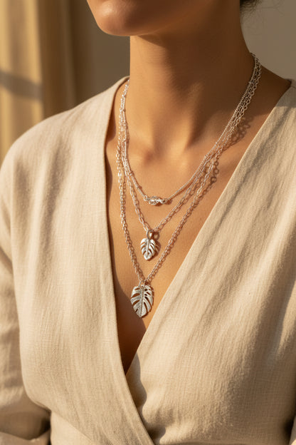 Layered monstera leaf charm necklace in white gold worn around the neck with a natural fiber top