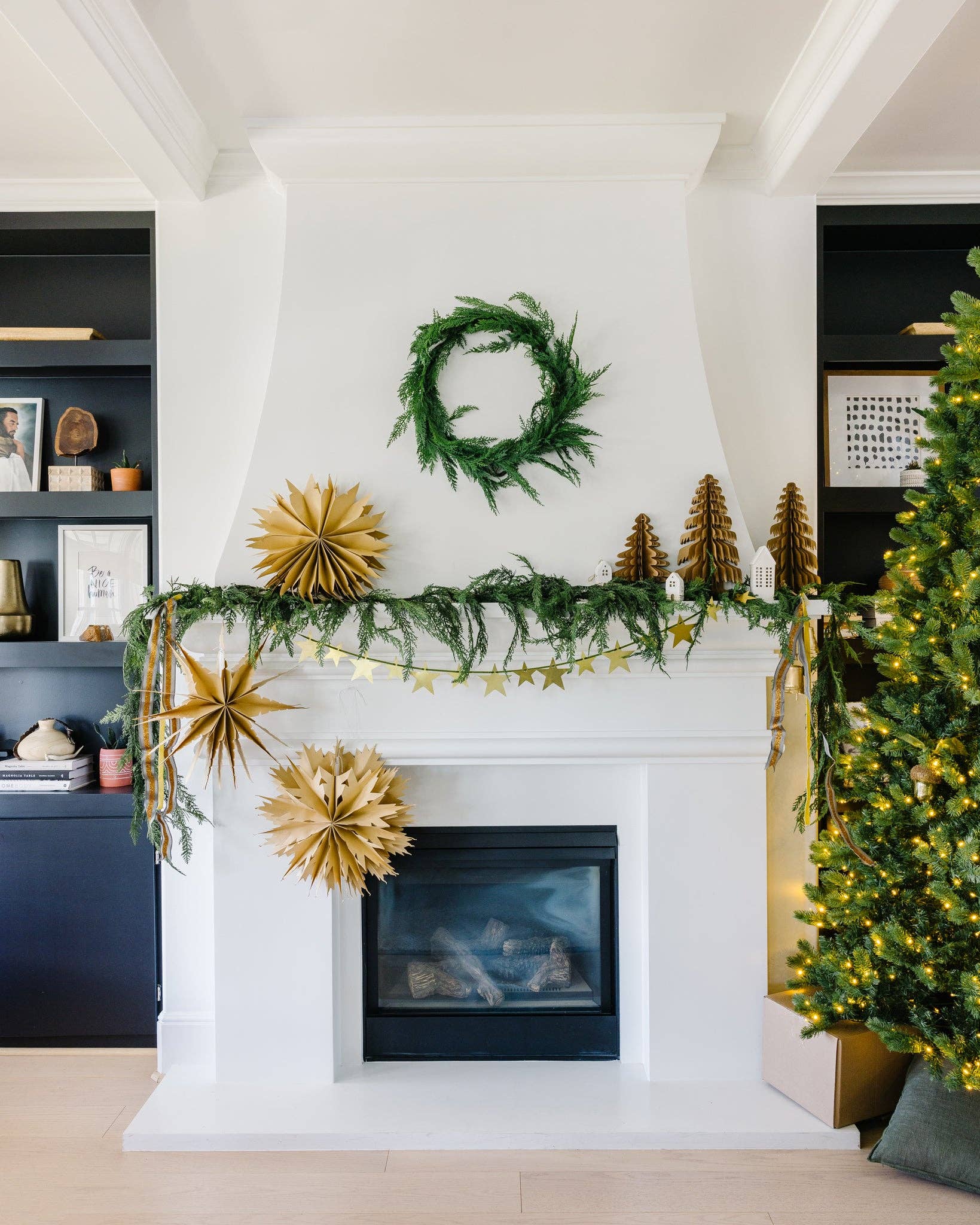 Decorated fireplace with greenery, gold ornaments, and a Christmas tree.