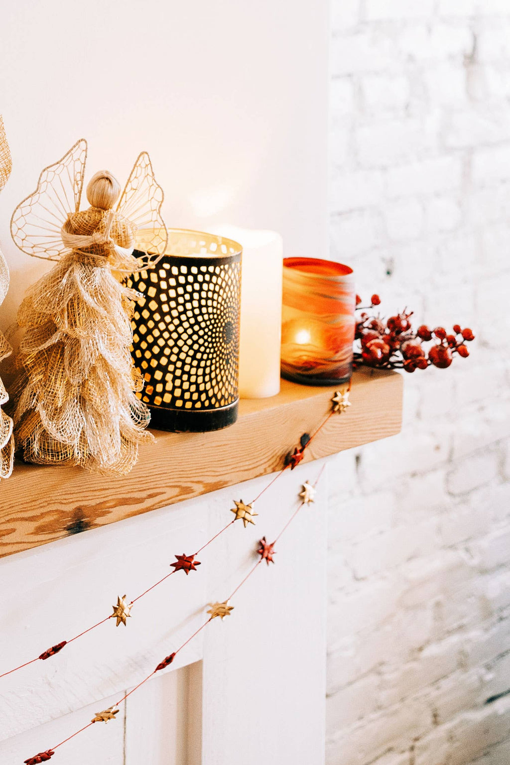 Decorative mantel with candles, a holiday fairy figurine, and festive decorations on a white background