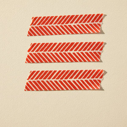 Three strips of red and white washi tape tape with a chevron pattern on a beige background.