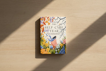 Book titled 'The Self Care Year' with a colorful cover featuring nature-themed illustrations on a white surface.