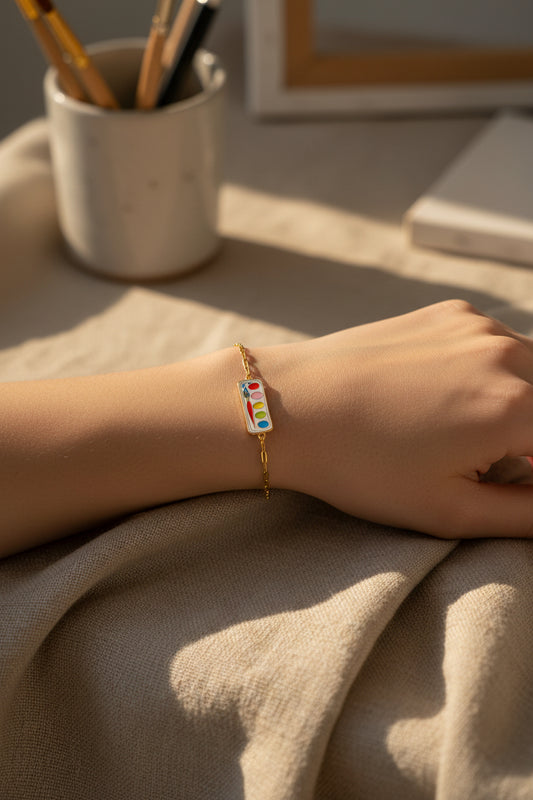 Gold bracelet with a colorful paint palette charm on a white background