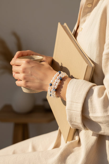 Person holding a notebook and a mug wearing a blue and white beaded bracelet from Rochambeau Home with a blurred background