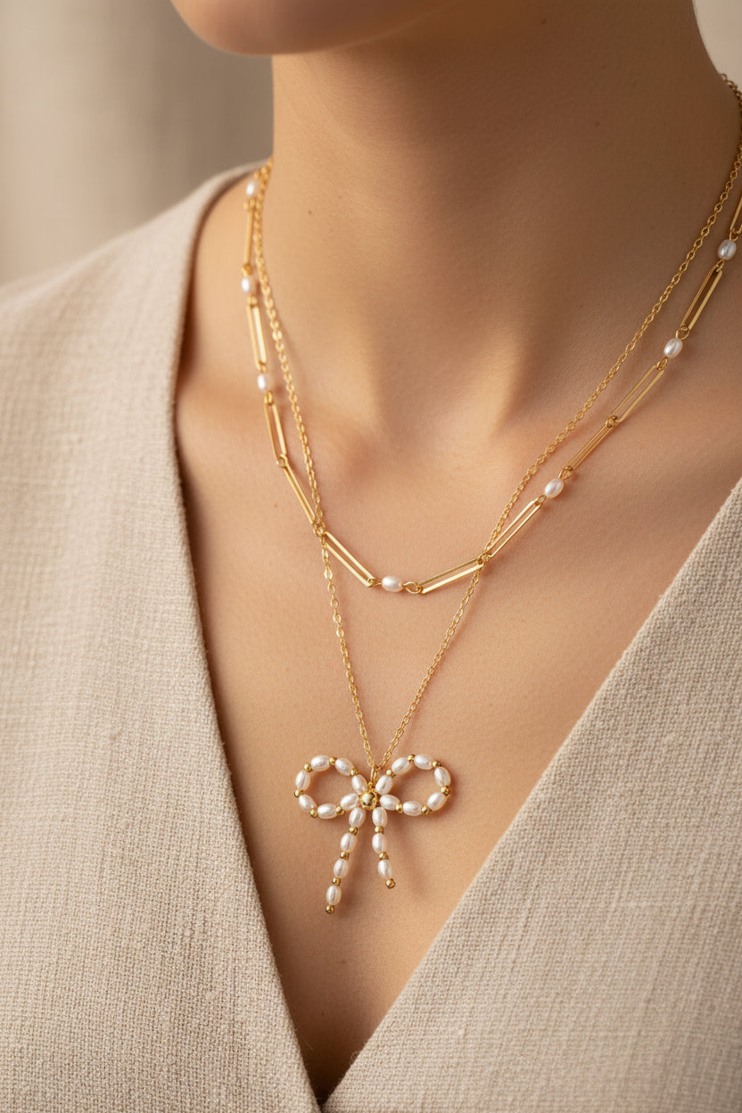 Necklace with a bow-shaped pendant worn by a person in a beige outfit.
