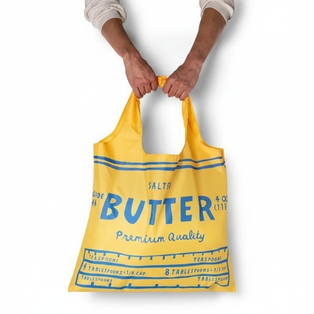Yellow tote bag with blue text held by a person on a white background
