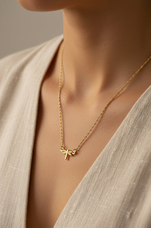 Gold necklace with a small dragonfly pendant being worn with natural garments and a light gray background
