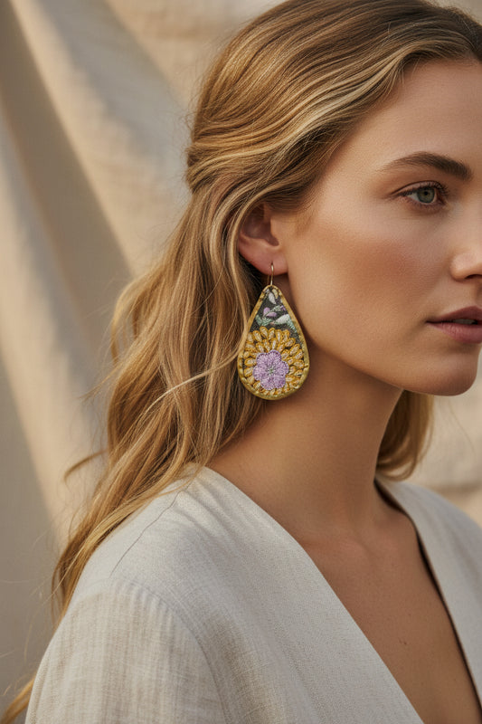Teardrop-shaped earrings with floral designs being worn on a white and beige background