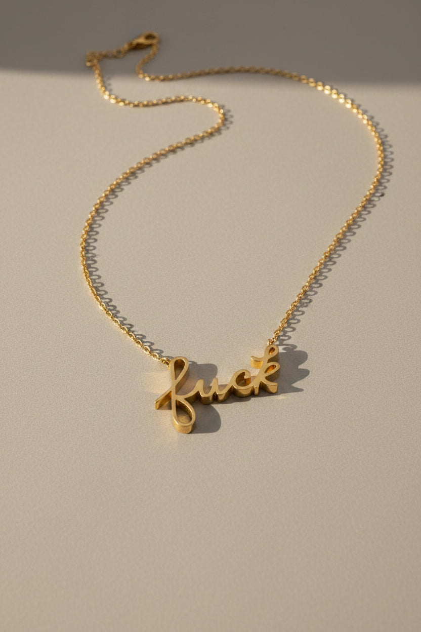 Gold necklace with a cursive 'fuck' pendant on a gray background