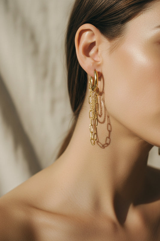 Gold chain earrings on a gold stand against a beige background