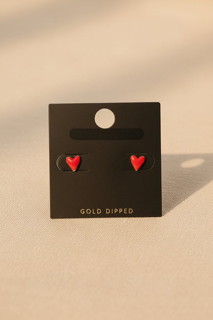 Red heart-shaped earrings on a black card with 'Gold Dipped' text, placed on a beige fabric background.