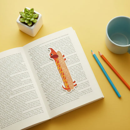 Hot Dog shaped bookmark laid on an open book with a small plant and stationery items on a desktop 