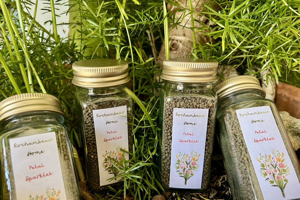 A 4 oz reusable glass jar labeled "Petal Sparkles," filled with a mix of wildflower seeds, featuring a gold tin lid—an eco-friendly gardening gift.