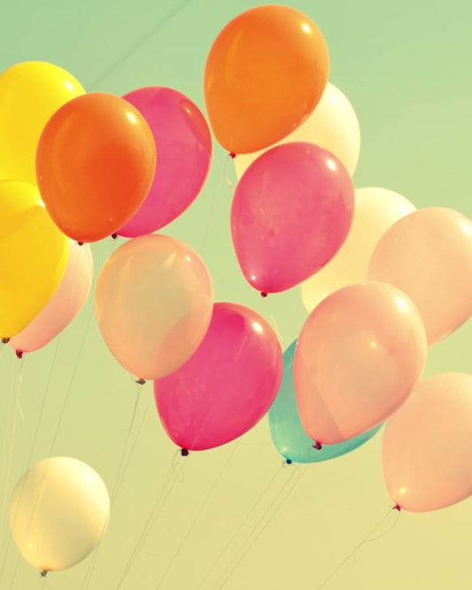 A floating collection of colorful balloons in shades of yellow, pink, orange, and blue against a light blue background, representing a festive or celebratory occasion.