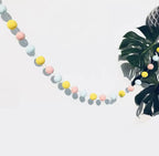 Felt ball garland draped across a pastel-themed nursery wall