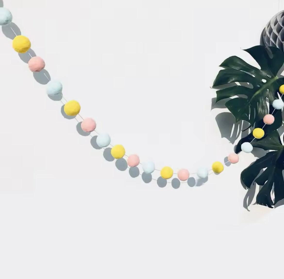 Felt ball garland draped across a pastel-themed nursery wall