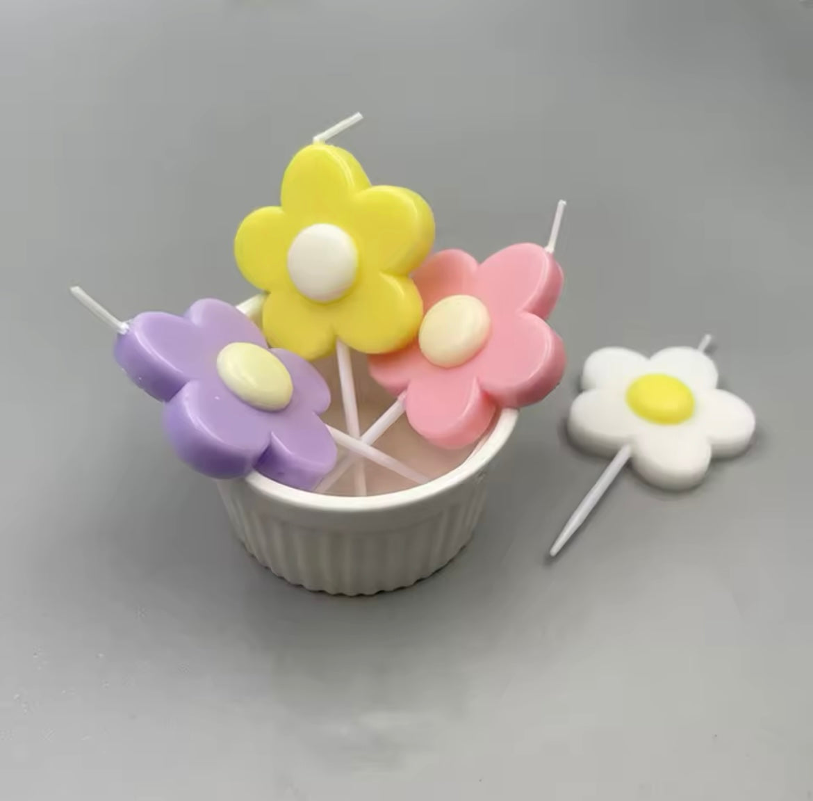 Daisy candles in purple, pink, green, and yellow showcased in a cup