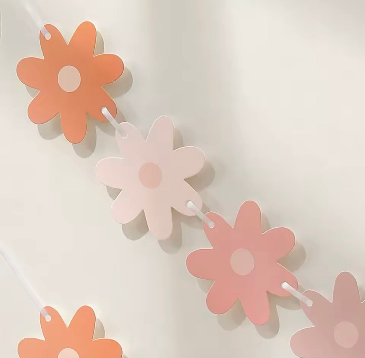 Pink gradient daisy paper banner strung across a soft pastel wall