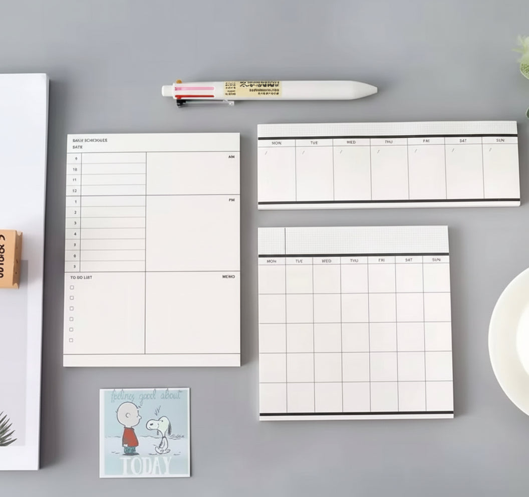 Monochrome monthly weekly daily planner notepads laid out on a desk top.