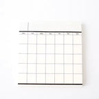 A monochrome weekly planner notepad with grid lines and headers for each day of the week displayed on a white background.