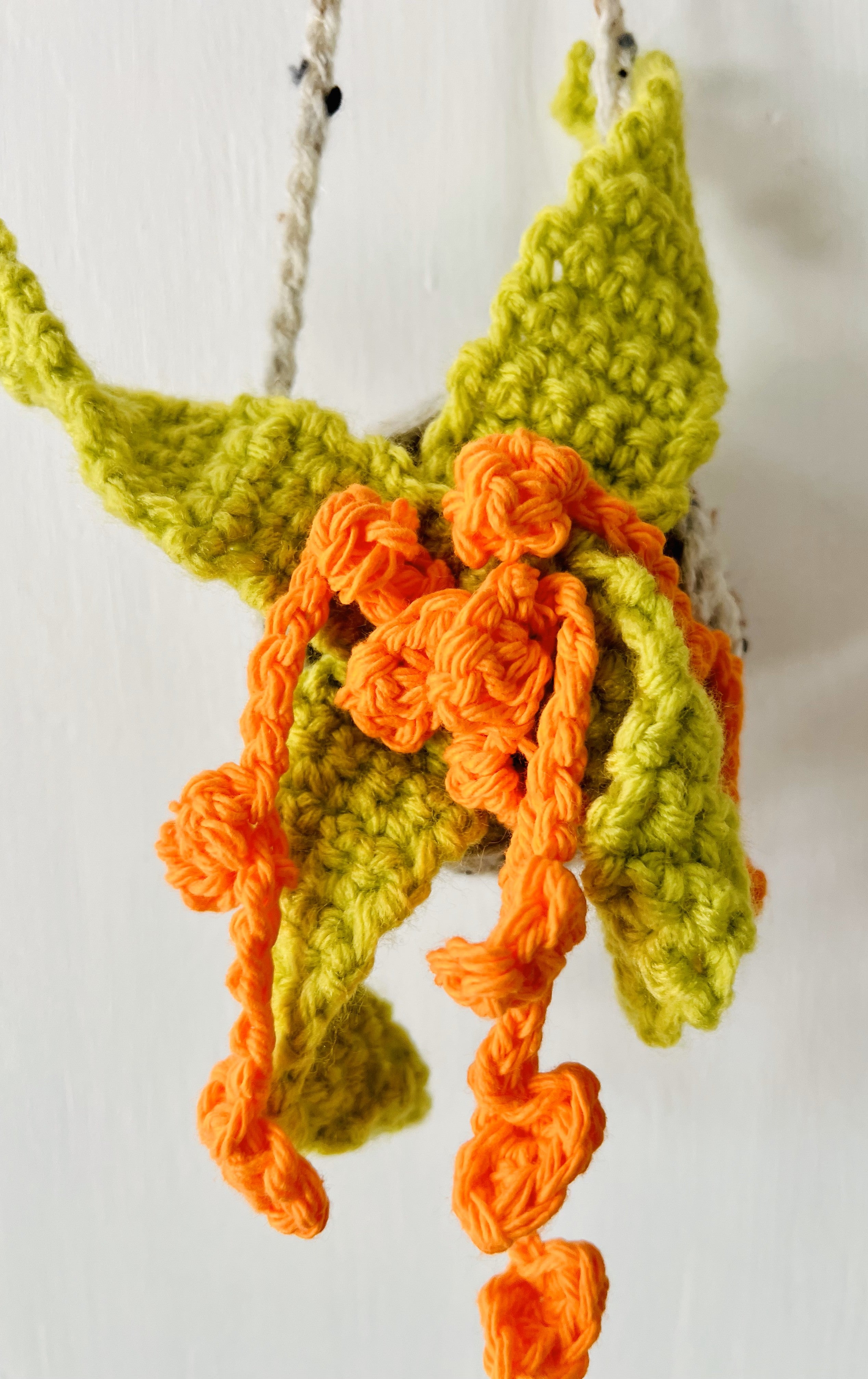Medium-sized crocheted air plant with bright green leaves and orange base, featuring trailing flowers