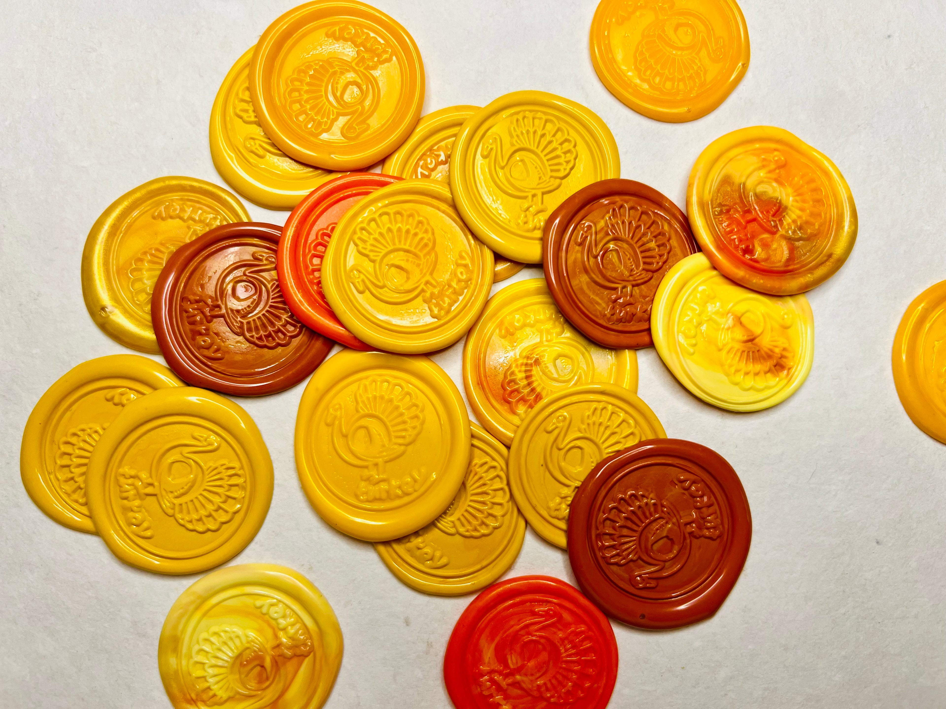 Assorted yellow and orange Gobble & Glow wax seal stickers in a pile on neutral handcrafted paper