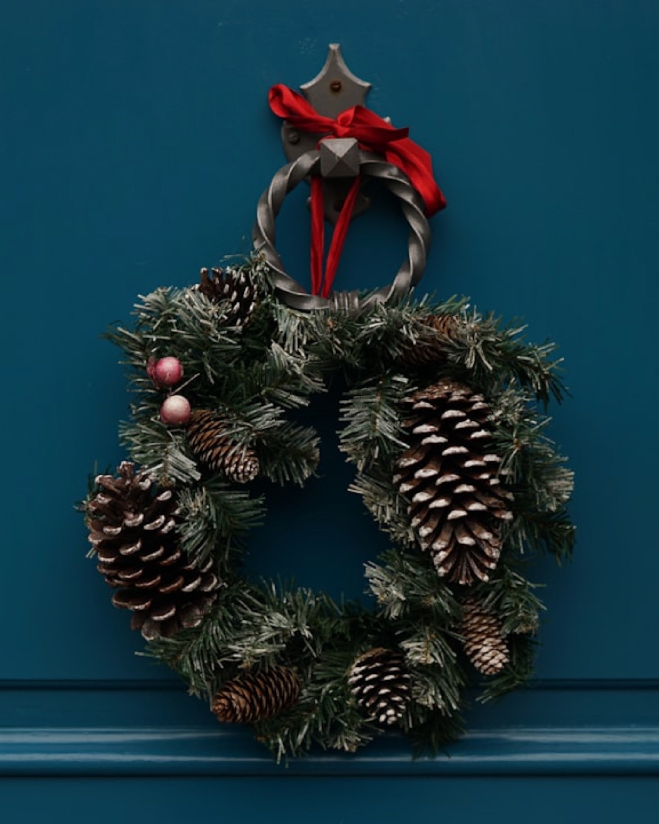 Christmas wreath with pine cones and red ribbons on a blue door