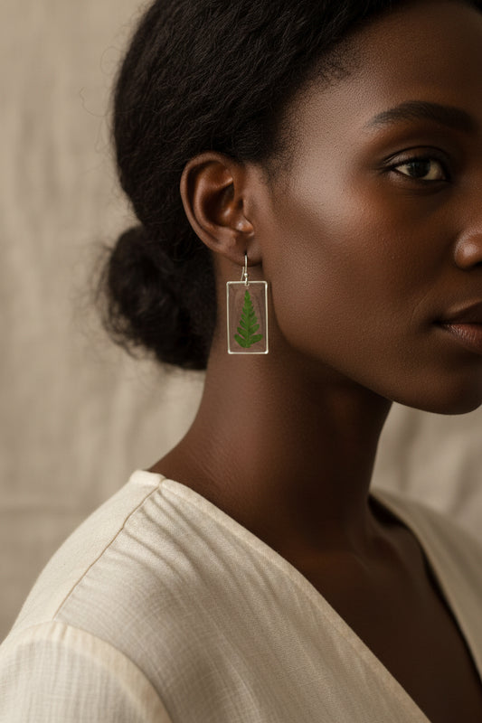 Fern leaves encased in resin and made into floral earrings being worn by a model with a neutral background
