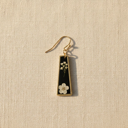 A single drop earring with a black background and small pressed white flowers pressed in resin