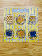 Set of six decorative magnets on a patterned card with 'Magnets' text, on a wooden surface.