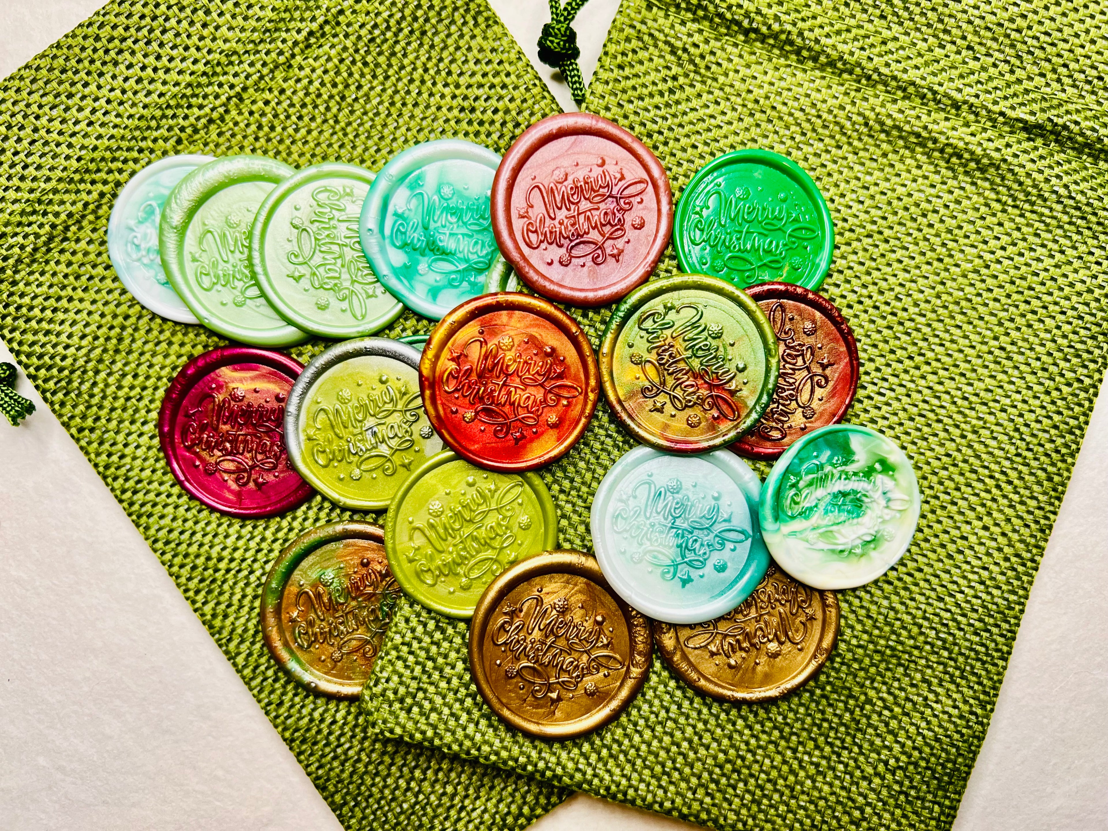 Colorful wax seal stickers with “Merry Christmas” embossed with tiny star details on two green burlap bags