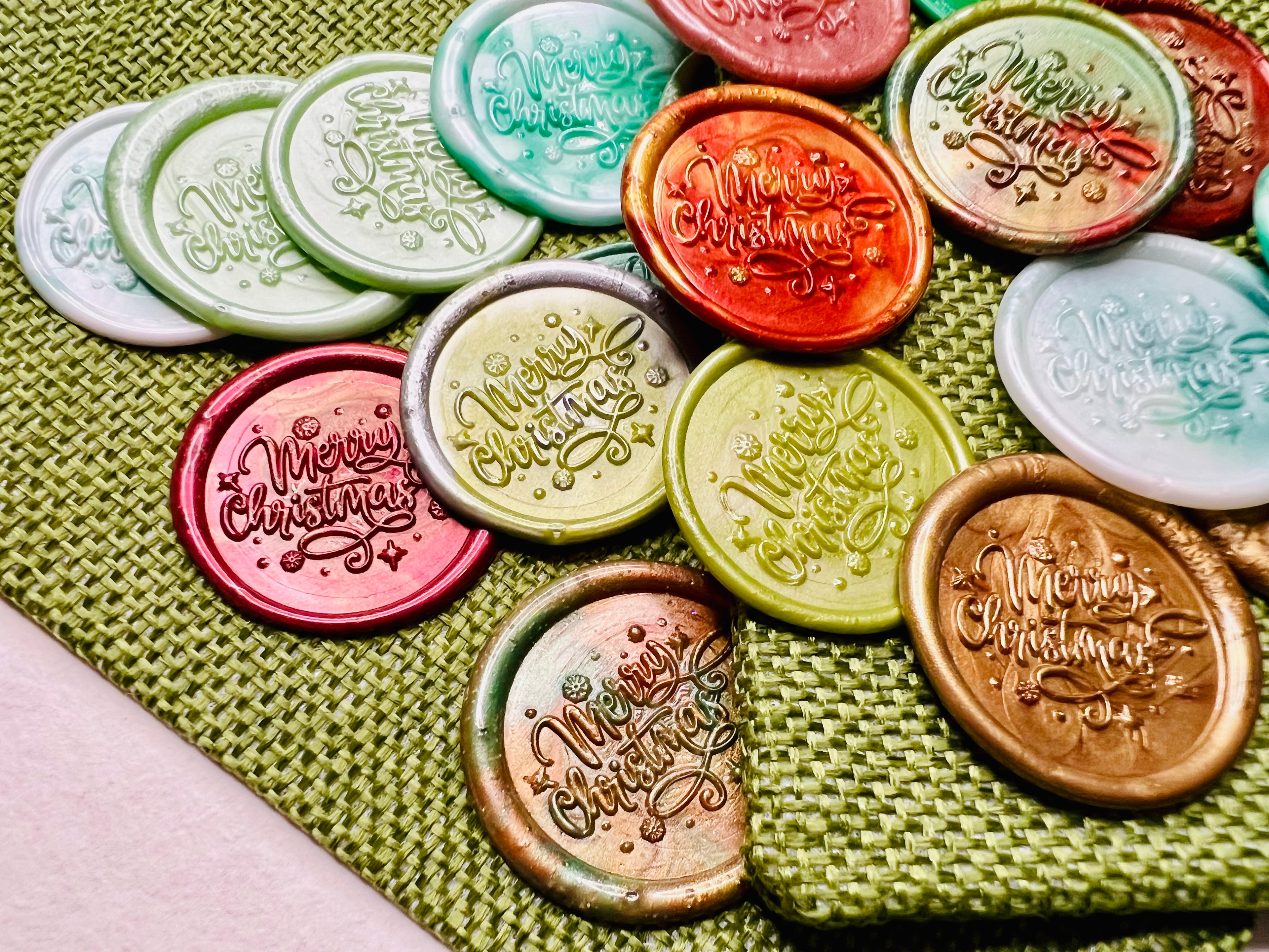 Close up view of “Merry Christmas” embossed wax seal stickers  with tiny star details and in various colors by Rochambeau Home.
