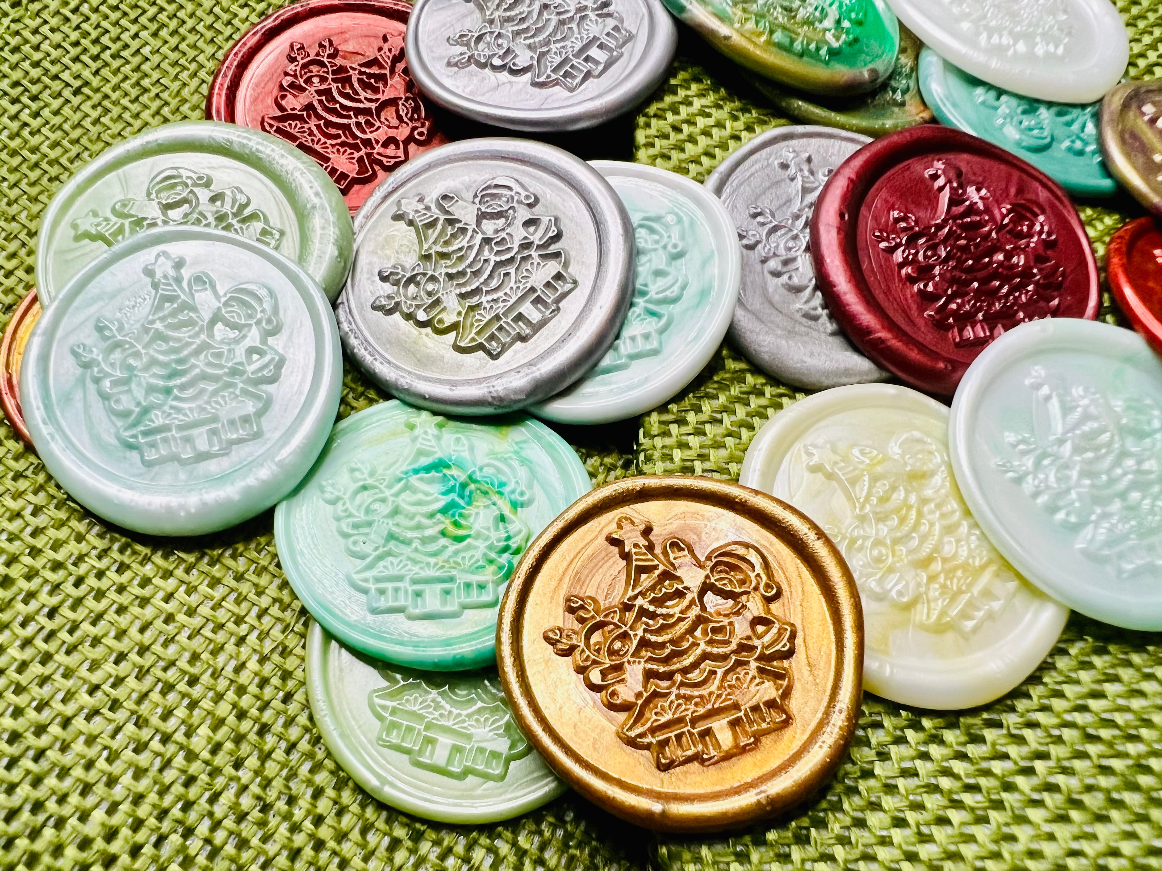 Various wax seal stickers with Santa beside a twinkling tree surrounded by wrapped gifts on a green burlap bags