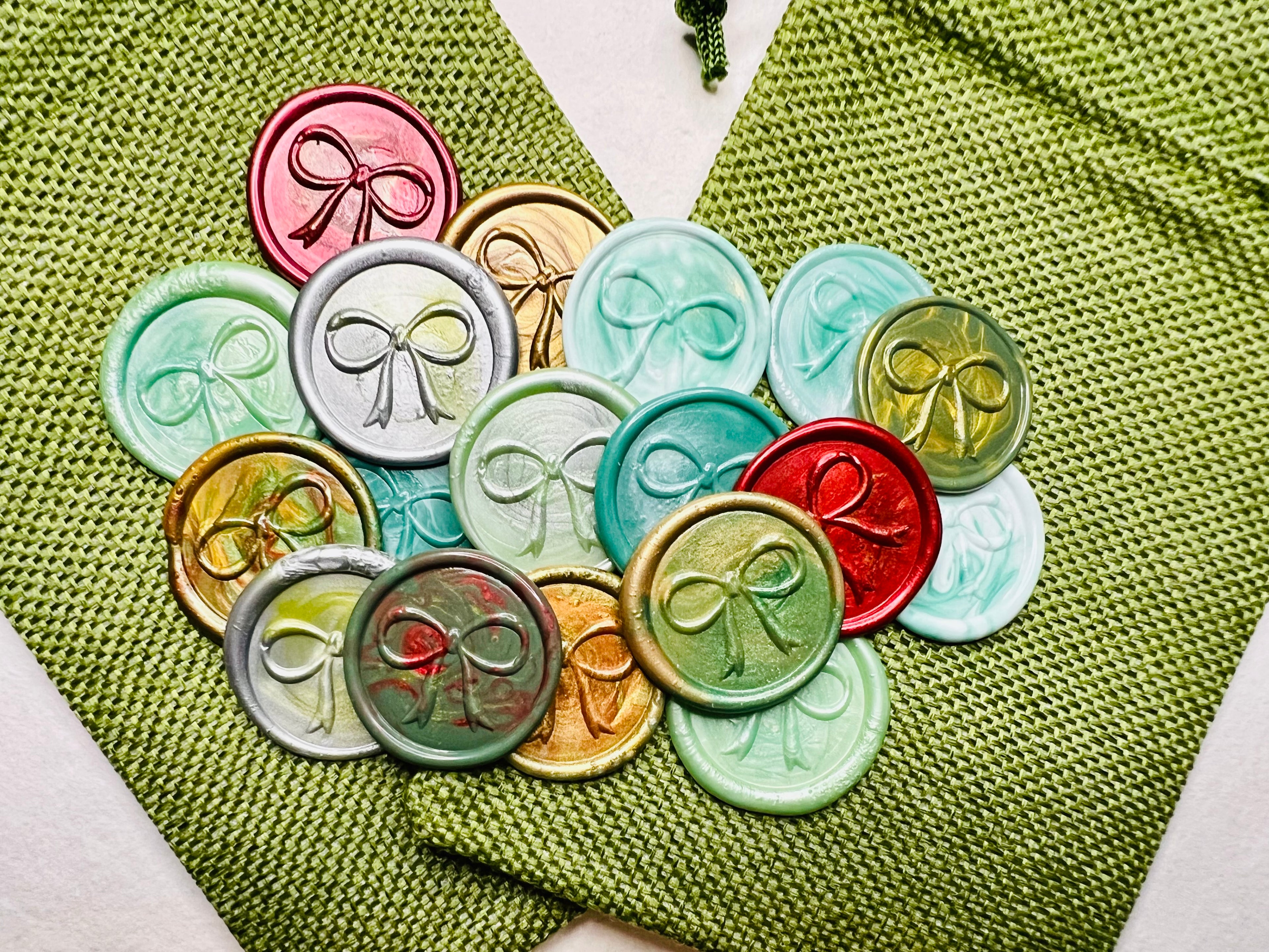 Festive Bow wax seal stickers created by Rochambeau Home in various colors  being showcased on green burlap bags.