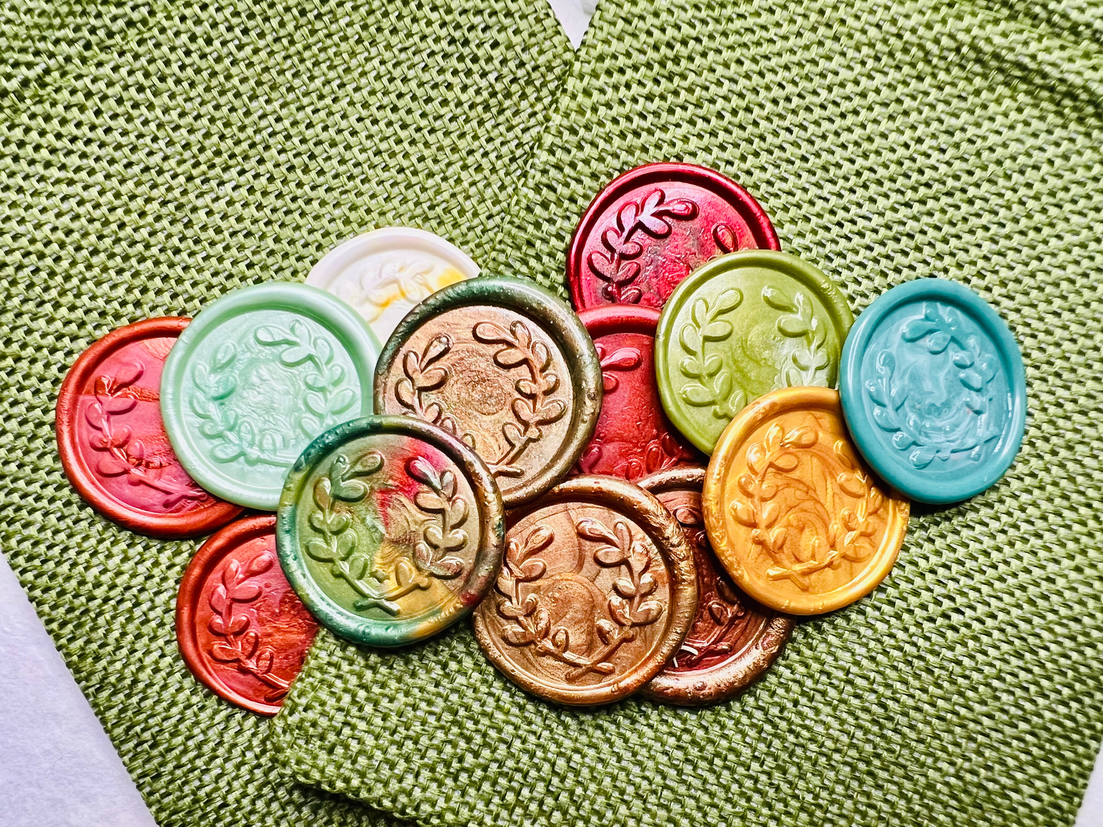 Seasonal Olive Branch Wreath wax seal stickers created by Rochambeau Home in various colors  being showcased on green burlap bags.