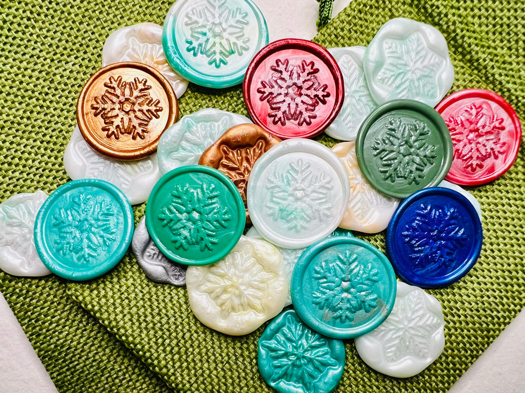 Festive Snowflake wax seal stickers created by Rochambeau Home in various colors  being showcased on green burlap bags.