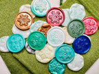 Festive Snowflake wax seal stickers created by Rochambeau Home in various colors  being showcased on green burlap bags.