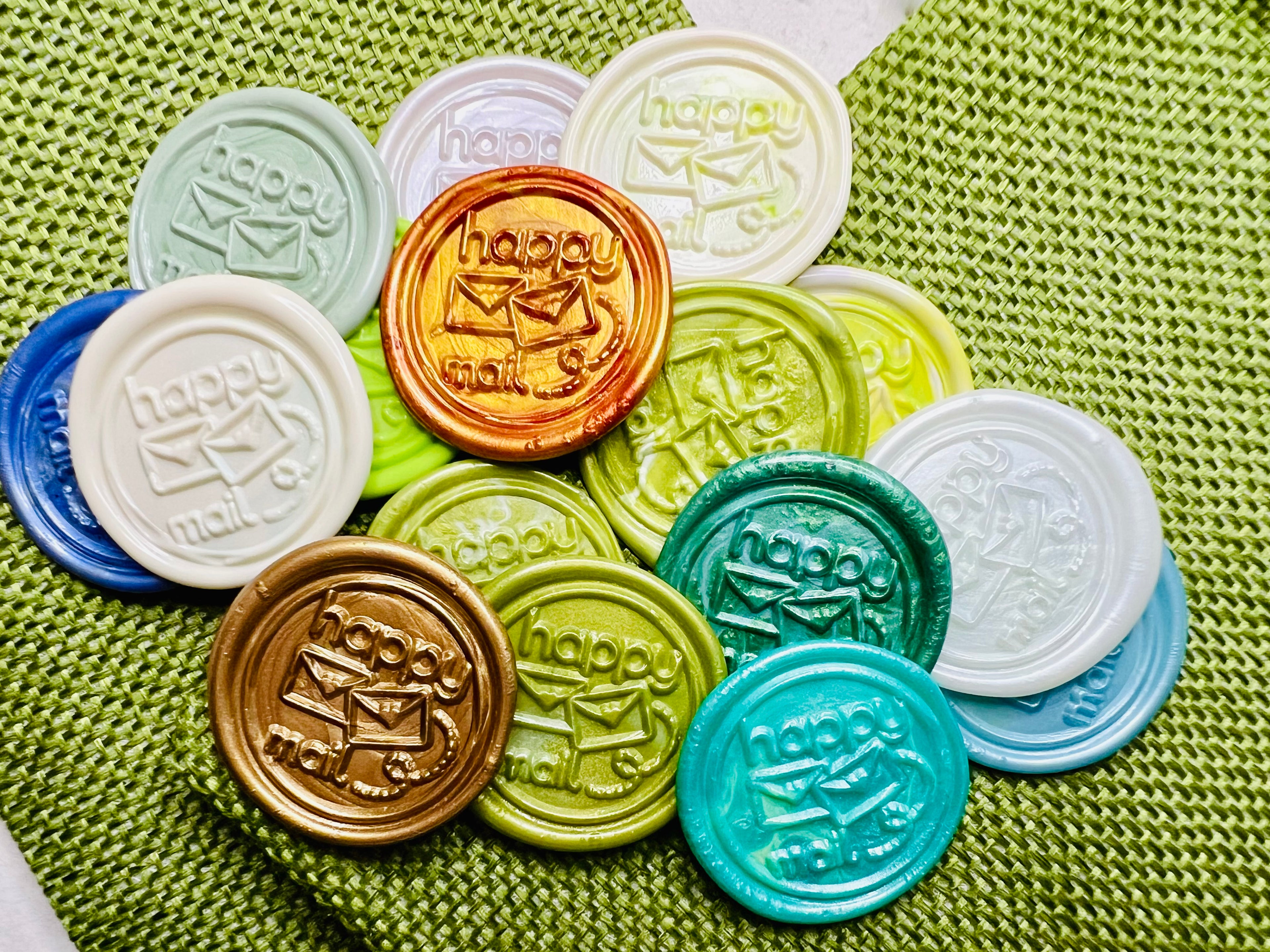 'Happy Mail' wax seal stickers created by Rochambeau Home in various festive colors showcased on green burlap bags.